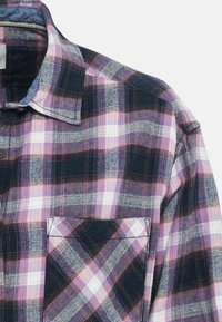 Chemise à carreaux aux couleurs rose, bleu marine, blanc et gris, avec un col et une poche avant sur un fond uni.