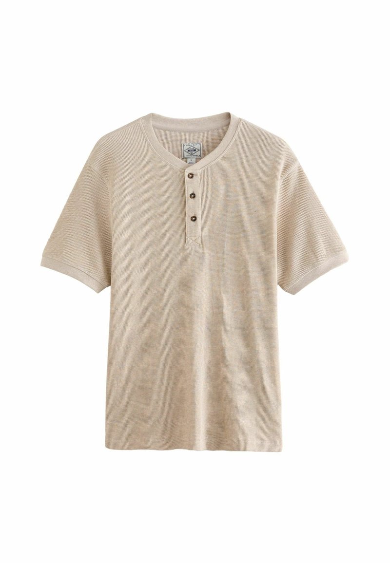 Camiseta henley de manga corta en color beige que presenta un tejido texturizado, cuello redondo y una tapeta de tres botones en la parte delantera.