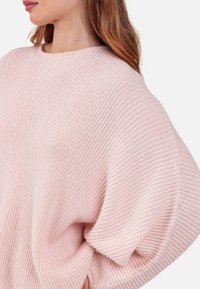 Pull oversize rose clair avec texture côtelée, encolure ronde et manches larges. Matière douce avec une coupe décontractée.