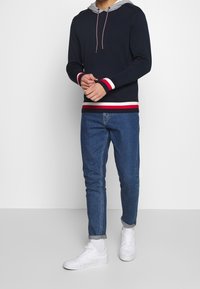 Merihenkinen huppari, jossa on harmaa huppu, punavalkoraitaiset hihansuut. Yhdistetty sinisiin slim fit -farkkuihin ja valkoisiin lenkkikenkkiin. Yksinkertainen muotoilu ja mukava istuvuus.