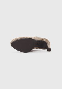 Chaussure à talon avec une tige texturée de couleur marron clair au motif reptilien. Semelle en caoutchouc noire avec un talon courbé. Éléments de design minimalistes.