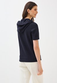Navy short-sleeve hoodie with a relaxed fit, featuring a textured fabric, slouchy hood, and a hem that falls at the waist.