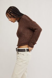 Καφέ πλεκτό πουλόβερ με ψηλό λαιμό, κοντό σχέδιο και υφή υφάσματος. Συνδυάζεται με λευκό παντελόνι και μαύρη ζώνη με ασημί λεπτομέρειες.
