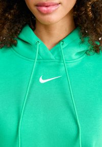 Green hoodie made of soft fabric, featuring a kangaroo pocket, drawstrings, and a white Nike logo on the chest.