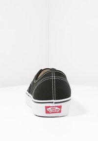 Baskets Vans noires vues de dos, avec surpiqûres blanches et semelle blanche avec un logo rouge "Off The Wall".