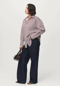 Camisa de cuadros en rojo y blanco, combinada con jeans de mezclilla anchos de color azul oscuro. Sosteniendo un pequeño bolso oscuro, lleva sandalias planas.