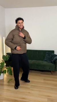 Brown checkered padded jacket with a high collar, front zipper, and side pockets, worn over black pants and shoes. Green couch in background.