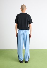 T-shirt preta de manga curta combinada com calças largas azul claro, apresentando riscas laterais pretas e uma cintura elástica. Calçado preto visível.