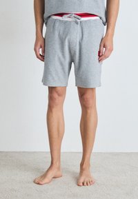 Graue Baumwollshorts mit einem elastischen Bund, ausgestattet mit einem Kordelzug, Seitentaschen und einem kontrastierenden roten und weißen Innenband.