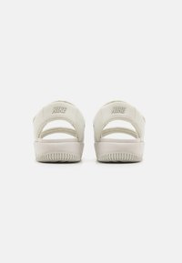 Valkoiset Nike-sandaalit, joissa on synteettinen päällinen, avonainen kanta ja teksturoitu kumipohja. Takana on Nike-logo kohotulostettuna.