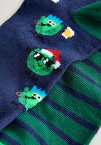 Daudzkrāsu zābaki ar karikatūriskiem zaļiem tēliem uz tumši zila fona un zaļiem svītrainiem elementiem. Mīksta auduma, sajauktas materiālu.