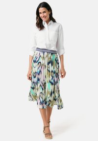 Weißes Hemd mit Knöpfen und zwei Brusttaschen, kombiniert mit einem plissierten, mehrfarbigen Midirock, der Muster in Grün, Blau und Pink aufweist.