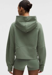 Cropped hoodie in gedempte groene kleur, met een gladde textuur, raglanmouwen en gestikte accenten. Gecombineerd met bijpassende korte broek.