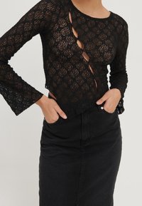 Haut noir en dentelle à manches longues présentant un motif floral, des découpes, et des manches évasées, associé à une jupe en denim noire.