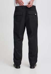 Svarte bukser med løs passform, med to baklommer og beltehempe, laget av teksturert stoff. Enkel design uten synlige mønstre.