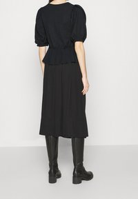 Top negro peplum con mangas abullonadas y un acabado texturizado, combinado con una falda larga negra y botas altas negras hasta la rodilla.