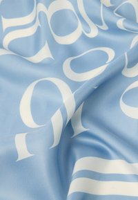 Svetlo modra tkanina z velikimi belimi grafičnimi črkami in črtami. Tekstura je videti gladka in rahlo sijoča.