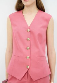 Gilet sans manches rose avec un décolleté en V profond, cinq boutons dorés et deux poches avant ; tissu lisse avec une coupe ajustée et un design minimaliste.
