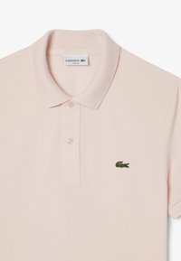 Ljust rosa polo skjorta i strukturerad tyg, med krage, tvåknapps knäppning och en grön krokodil-logga på vänster bröst.