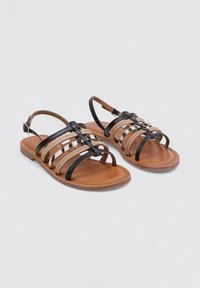 Sandalias slingback con tiras sintéticas negras, detalles en beis tejidos y una suela marrón con un diseño plano. Incluye un detalle decorativo de hebilla.