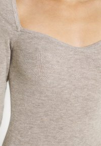 Haut en tricot côtelé beige avec un décolleté large et un discret panneau de poitrine. Texture douce avec une silhouette ajustée.