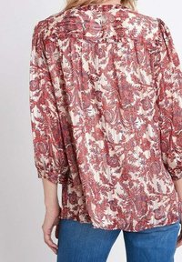 Pusero med en krämfärgad bas och intrikata röda och blå paisleymönster. Har en avslappnad passform, puckade ärmar och en plisserad bakdesign.