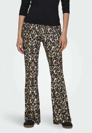 Pantalons évasés à imprimé léopard avec une texture soyeuse, fond beige et taches marron foncé, associés à un pull noir à côtes et des chaussures noires.