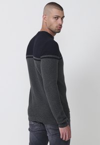 Suéter para hombres con un diseño texturizado que presenta franjas horizontales en gris oscuro, azul marino y gris claro a lo largo de los hombros. Puños y dobladillo acanalados.