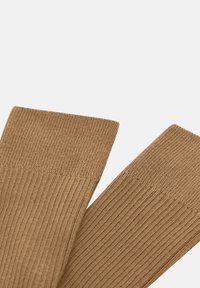 Calcetines marrones con canalé y una textura suave, con un puño ligeramente más ancho. La tela es elástica y está diseñada para un ajuste cómodo.
