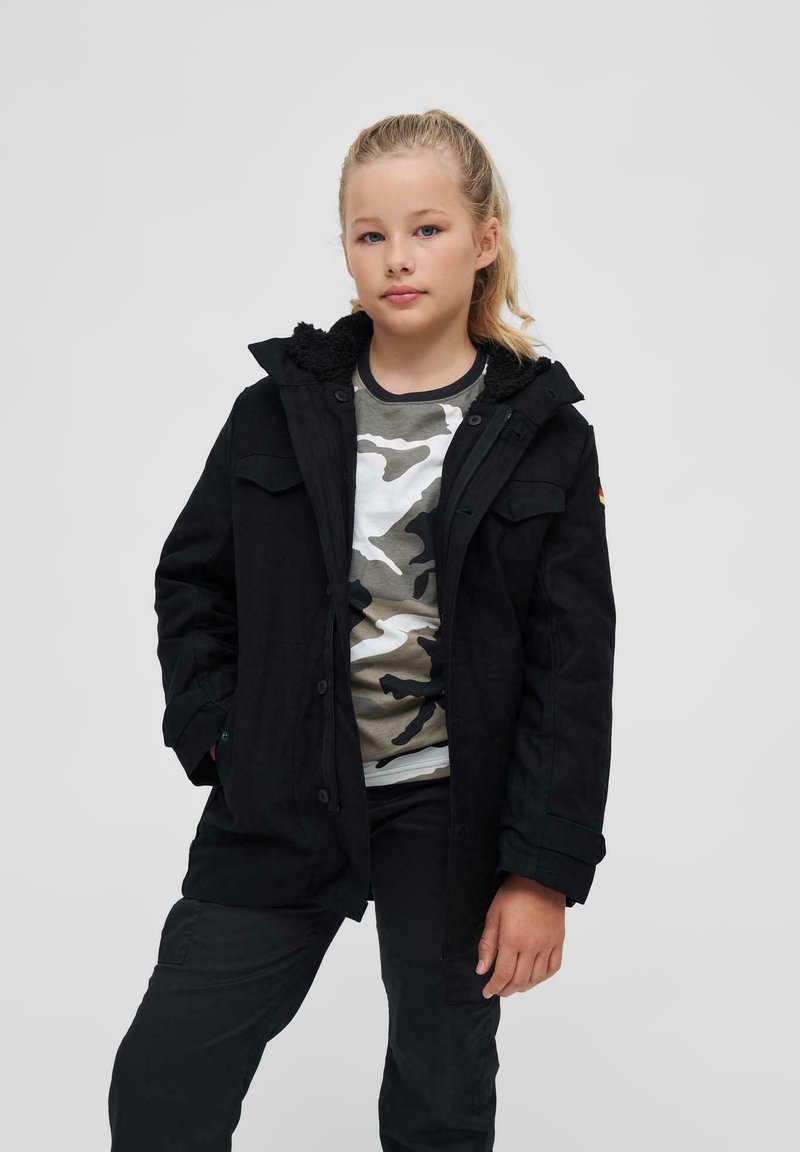 Črna jakna z kapuco obloženo s krznom, z več žepi, nosi se čez srajco z vojaškim vzorcem in črne hlače.