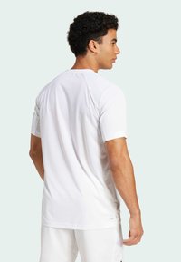 Short-sleeved athletic shirt in white, featuring a textured fabric, raglan sleeves, and a subtle logo near the hem.