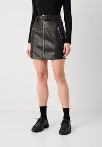 Černá kožená mini sukně s předním zipem, šikmými kapsami na zip a širokým páskem. Má přiléhavý design a hladkou texturu.