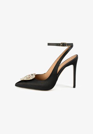 Črne satenske stiletto čevlje z ostrim nosom, trakcem okoli gležnja in velikim okrasjem z dragulji spredaj. Gladka tekstura, sijoča površina.