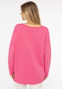 Maglione a maniche lunghe, taglio morbido, di un vivace rosa con un collo rotondo. Presenta un bordo giallo a contrasto sul collo e una texture morbida.