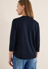 Haut bleu marine à manches longues avec un col ras du cou, fabriqué en matière douce. Présente une coupe droite et des accents d'ouverture latérale.