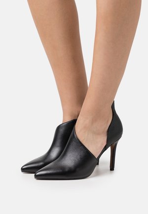 Schwarze Lederhochhackige Schuhe mit spitzen Zehen, Ausschnitten an den Seiten und strukturierten Akzenten nahe der Ferse.