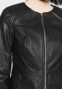 Giubbotto in pelle nera con collo rotondo, zip frontale e dettagli cuciti. Ha tasche laterali e una texture liscia.