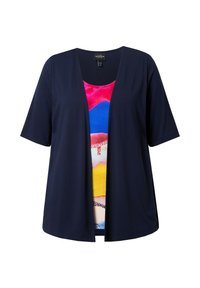 Námořnická modrá otevřená halenka s krátkým rukávem, která je vrstvená přes barevný tank top se vzorem v růžové, modré, žluté a bílé.