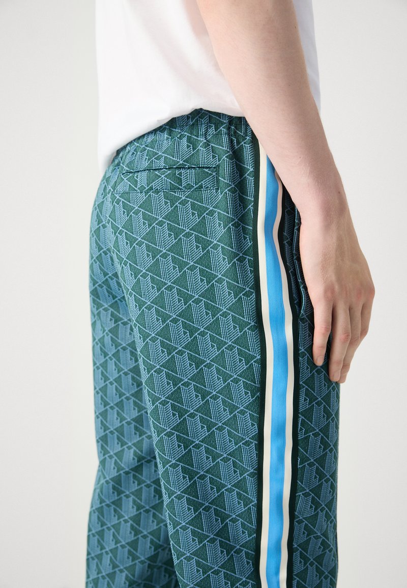Pantalons verts à motif géométrique, avec une bande latérale bleu clair et des accents crème, ceinture élastique, et détail de poche arrière.