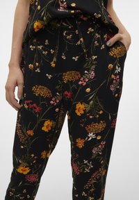 Pantalon noir à fleurs avec une variété de fleurs colorées en orange, rose et blanc, doté d'une taille élastique et de poches latérales.
