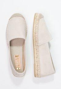 Scarpe espadrillas beige realizzate in suede con un accento in juta intrecciata attorno alla suola, caratterizzate da un design slip-on e una fodera in tessuto morbido.