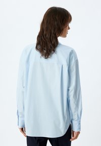 Camicia button-up azzurro chiaro con un fit rilassato, maniche lunghe e dettagli sui polsini; texture liscia, cucitura del giromanica sul retro e orlo curvo.