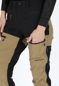 Swedemount broek in zwart en bruin, met ritszakken, een elastische tailleband en een mix van texturen op de stof.