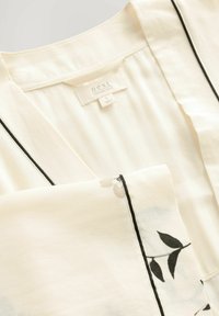 Lekki kremowy kimono z czarnym konturem i kwiatowym nadrukiem. Materiał ma gładką teksturę i luźny krój, z metką oznaczoną "next."