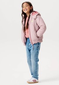 Ljusrosa kviltad pufferjacka med huva, rosa foder och dekorativ märke. Bärs över en rosa skjorta och ljusblå jeans. Vita sneakers.
