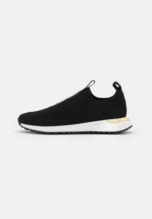Czarny dziany sneaker slip-on z białą podeszwą i złotym akcentem na pięcie, wyposażony w pętelki na języku i pięcie dla łatwego zakładania.