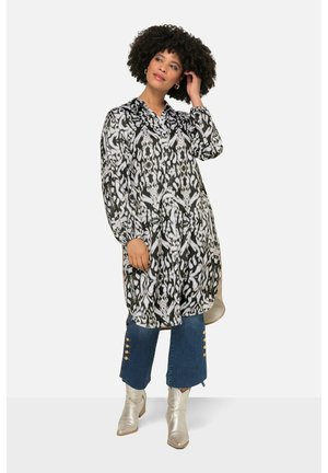 Blouse à motif noir et blanc avec des manches longues, design col, et coupe ample, associée à un pantalon en denim court avec des boutons dorés et des bottines argentées brillantes.