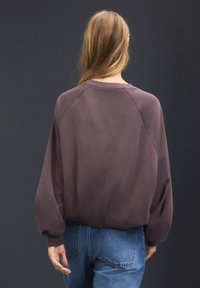 Overdimensioneret lilla sweatshirt med raglanærmer, rundet halsudskæring og ribkant på ærmerne. Båret med højtaljede blå jeans.