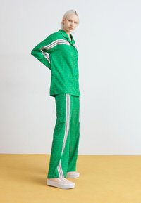 Green patterned two-piece outfit featuring a button-up shirt and trousers with white stripes, made of lightweight fabric.