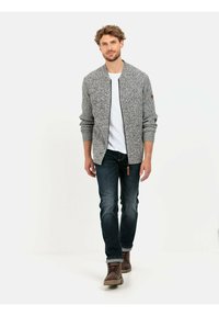 Graue, strukturierte Bomberjacke mit gerippten Manschetten und Kragen, getragen über einem weißen T-Shirt und kombiniert mit dunklen Jeans und braunen Stiefeln.